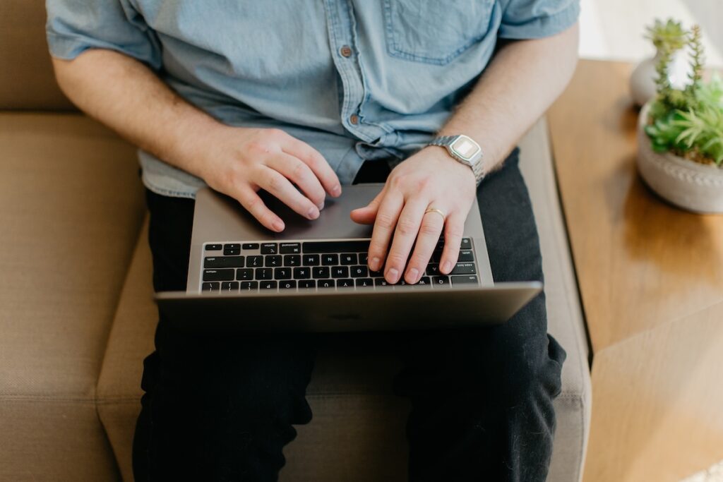 man typing on a Macbook wearing a denim shirt